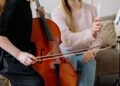 Aluno tocando guitarra elétrica em aula com o professor corrigindo a posição da mão